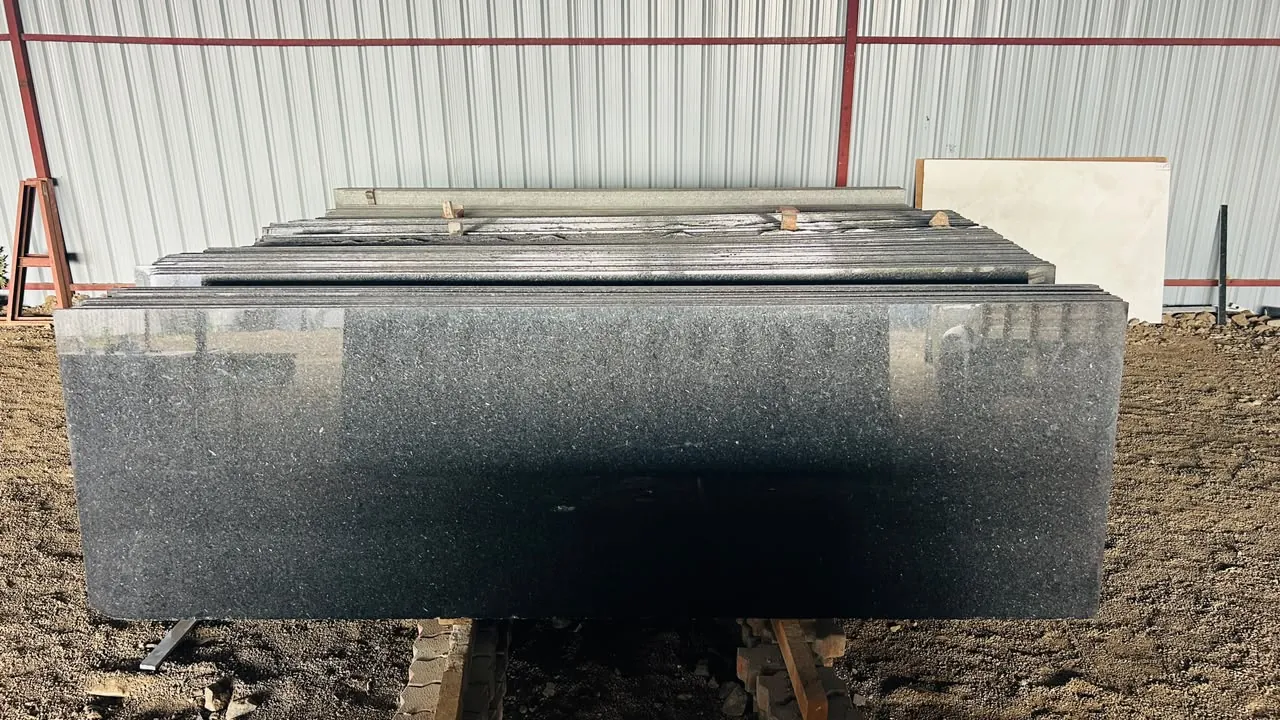 Polished black granite slab with a stack of matching slabs behind it